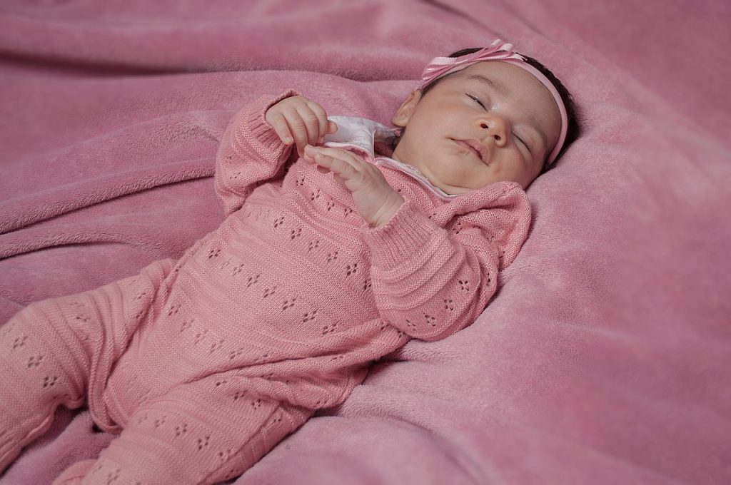 A serene baby girl peacefully sleeping on a cozy pink blanket, dressed in pink knitwear.